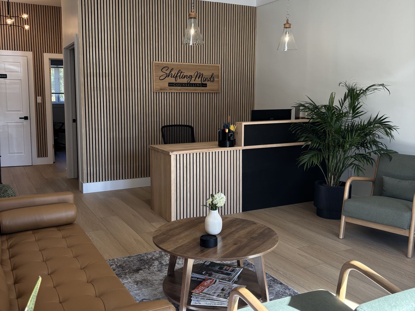 The Shifting Minds waiting room: a sign on a slatted wood wall behind the reception desk, a leather sofa, armchairs and plants